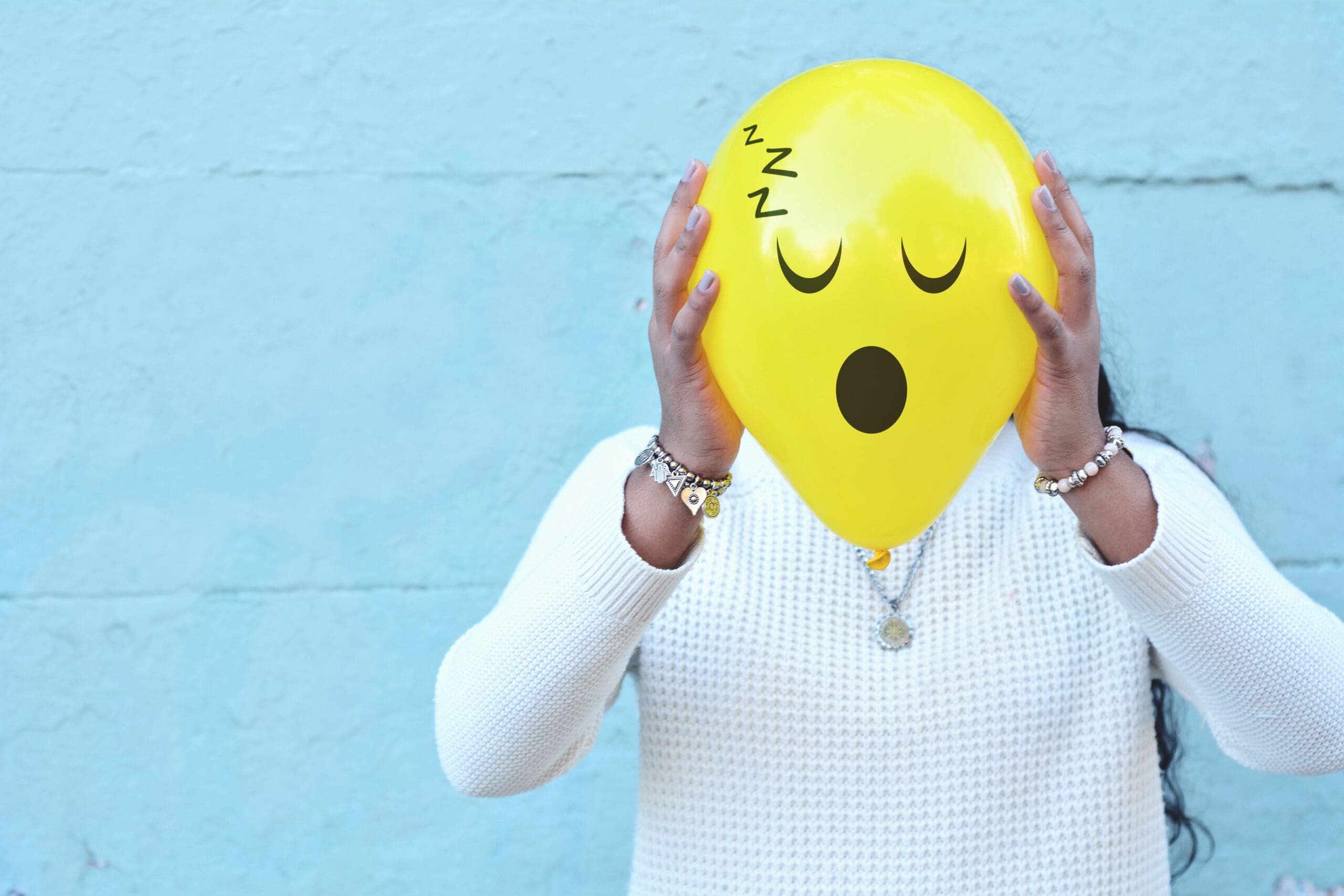 A woman snoring while holding a yellow balloon with a sad face on it.