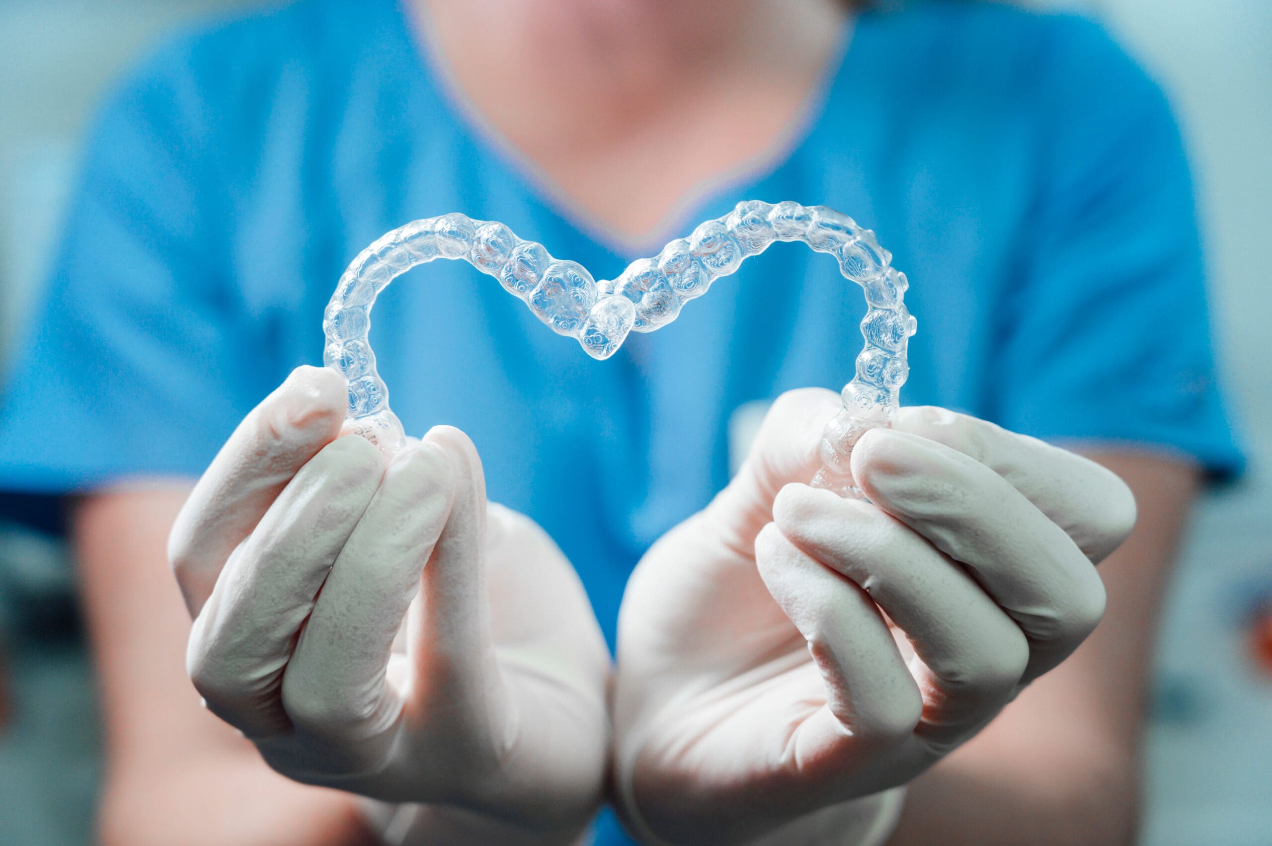 A dentist showcasing invisalign clear aligners with a heart shaped brace.