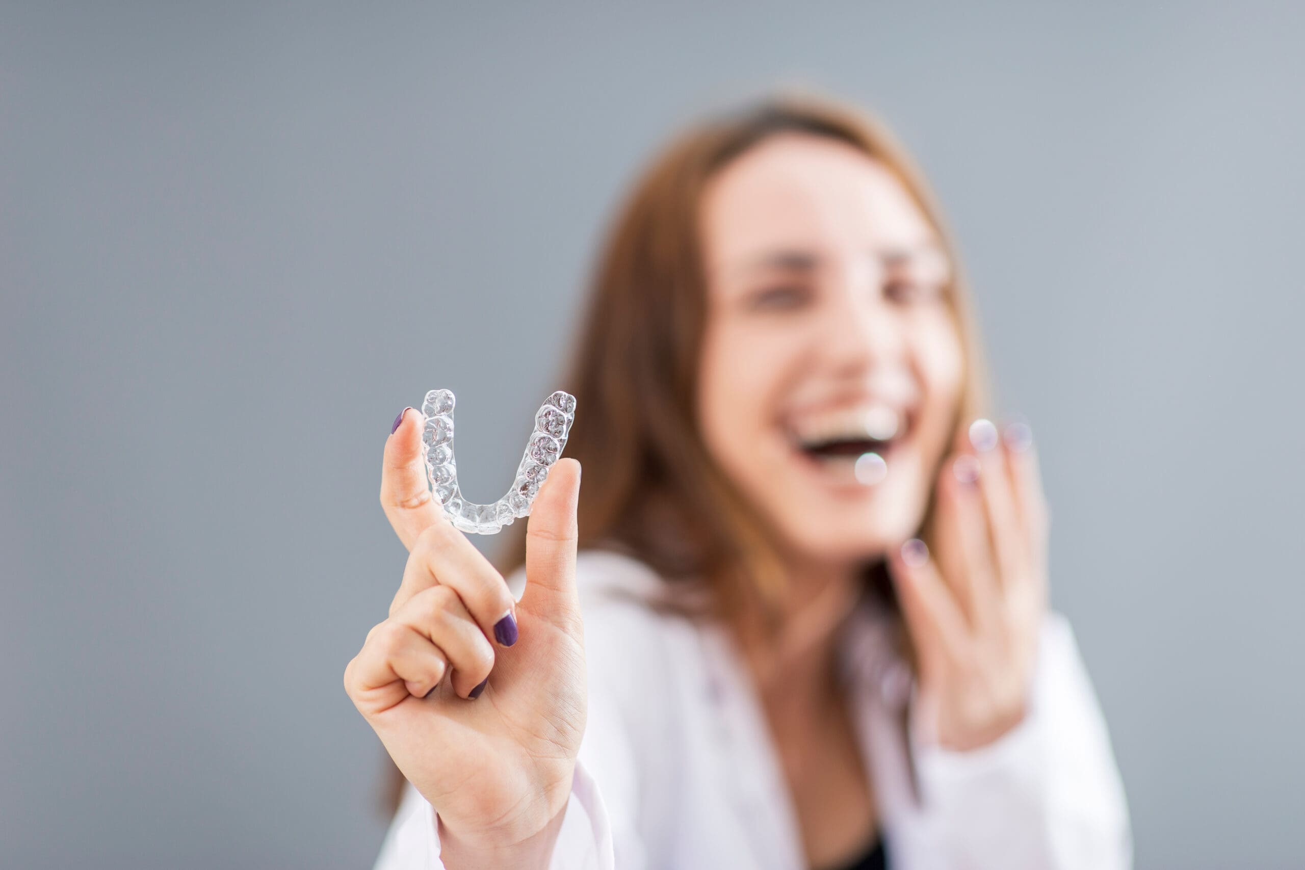 A woman is holding an orthodontic aligner in front of her face.
