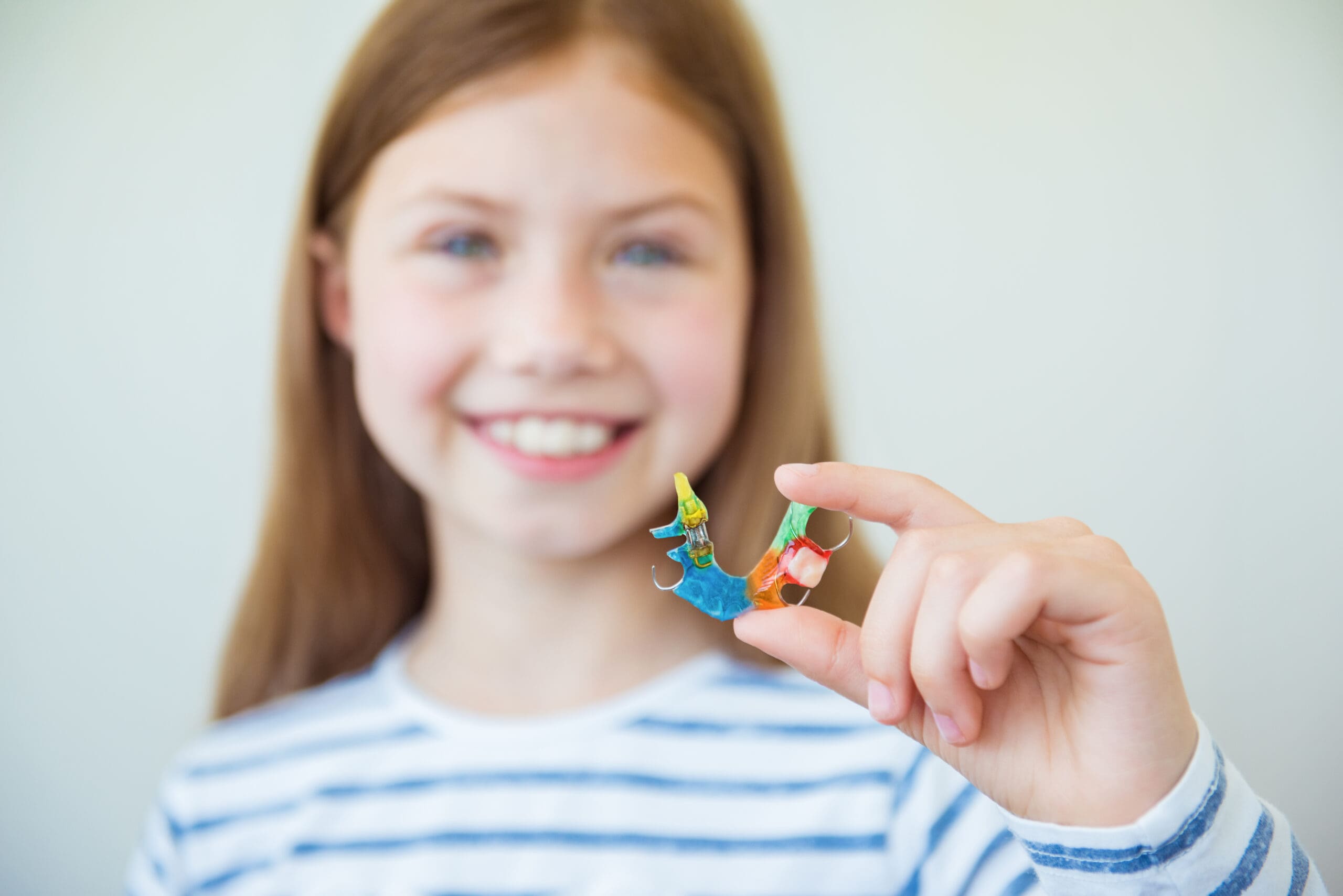 A young girl showcasing her orthodontic process with a small origami model.