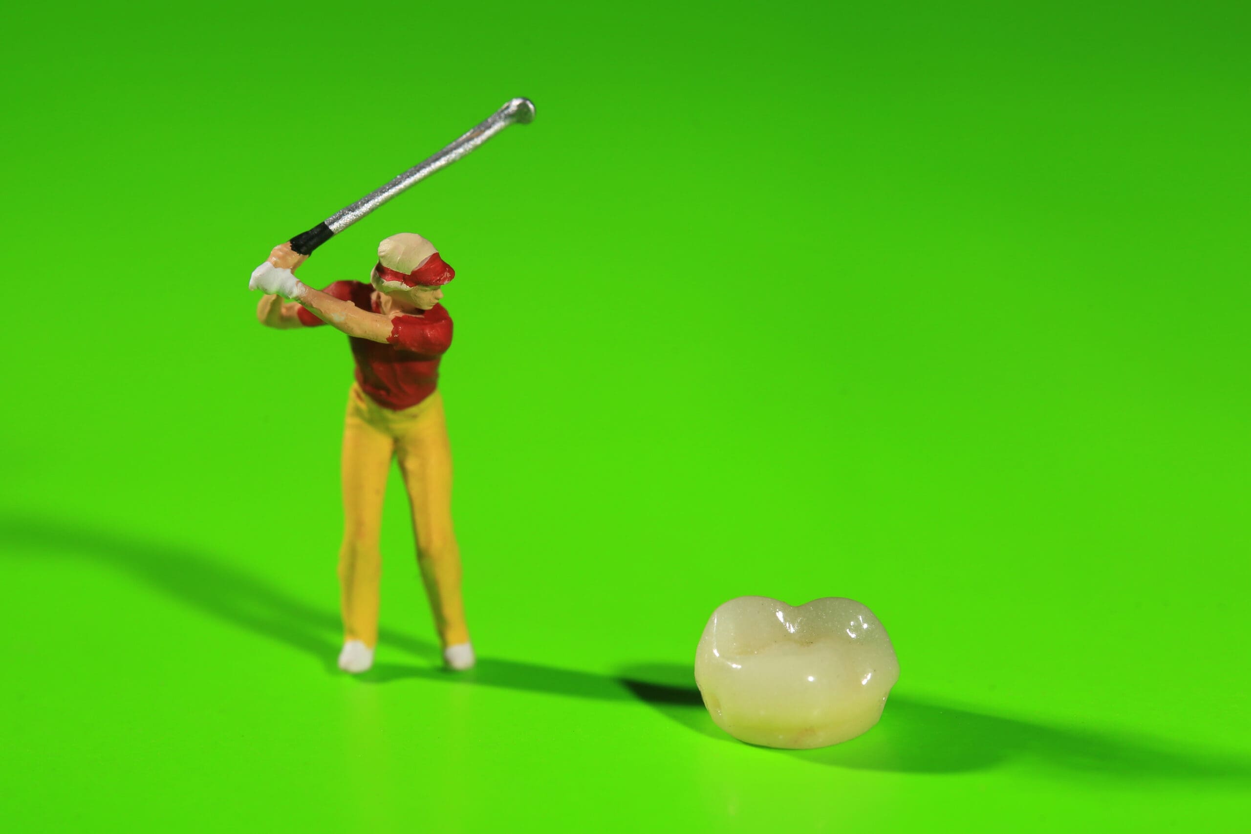 A tooth-wielding toy golfer on a green background.