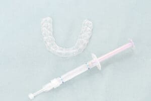 A dental syringe and a tooth brush on a blue background for teeth whitening.